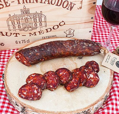 Chorizo pur bœuf mi-fort 100% maison sur un rondin de bois une nappe rouge et blanche vichy et une caisse de vin bois en arrière plan