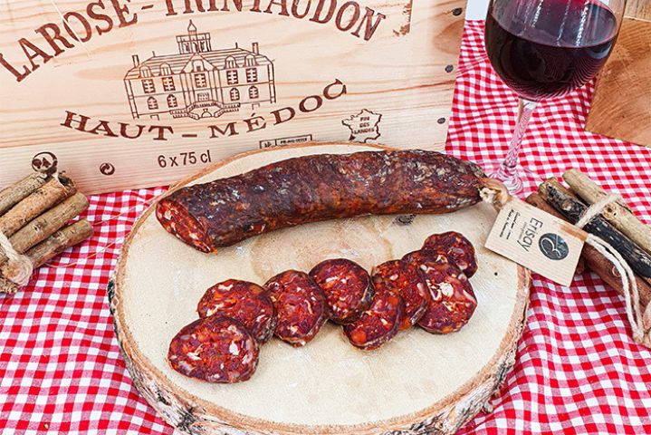 Chorizo pur bœuf maison BD Chorizo pur bœuf mi-fort 100% maison sur un rondin de bois une nappe rouge et blanche vichy et une caisse de vin bois en arrière plan