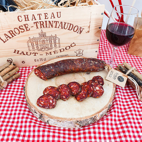 Chorizo pur bœuf mi-fort 100% maison sur un rondin de bois une nappe rouge et blanche vichy et une caisse de vin bois en arrière plan