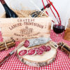saucisson sec de porlin maison découpé sur un rondin de bois posé sur une nappe vichy rouge et blanche, un verre de vin et une caisse de vin en bois.