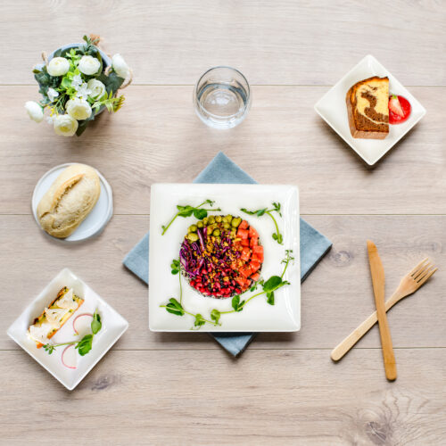 Plateau repas présenté sur un fond bois avec couverts, pain entrée, plats, desserts et petit bouquet de fleurs