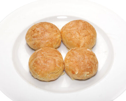 4 Chou gougère au fromage posés sur une assiette rond en porcelaine blanche sur fond blanc