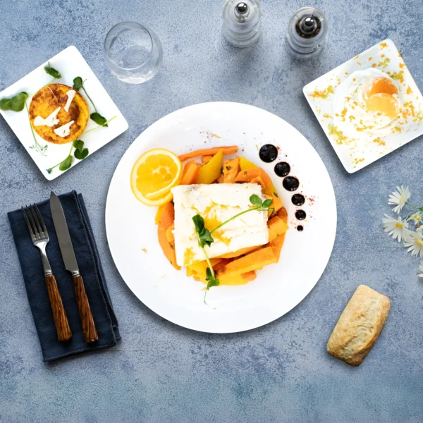 Le plateau repas poisson sans gluten "Les Arcs" est composé d' un clafoutis de chou-fleur et gorgonzola, d'un filet de sébaste à l'orange, d'une poêlée de légumes racines, de fromage d'une pavlova aux agrumes. Pour finir, un petit pain avec du gluten. Présenter sur un fond marbre.