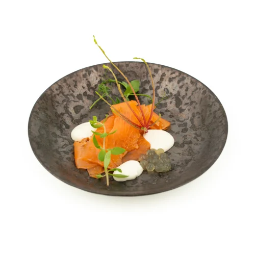Saumon fumé maison et crème yuzu dans une assiette noir sur fond blanc