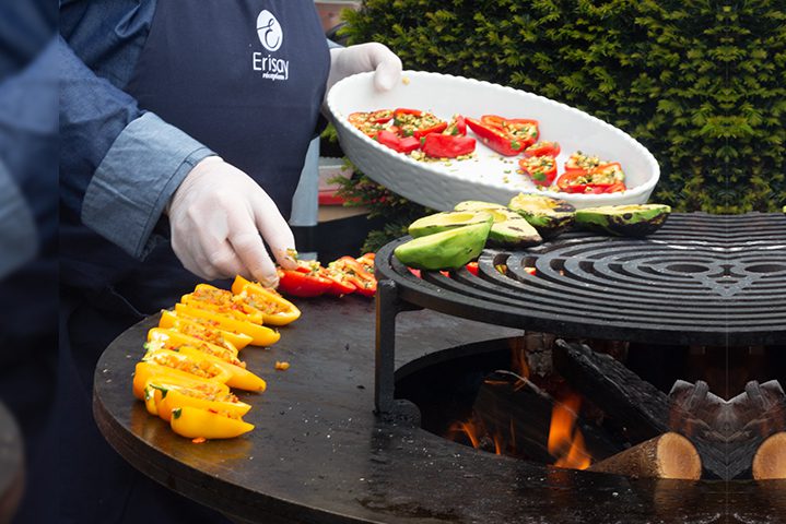 Cuisinier portant un tablier ERISAY Réceptions en train de faire griller des légumes sur un braséro.