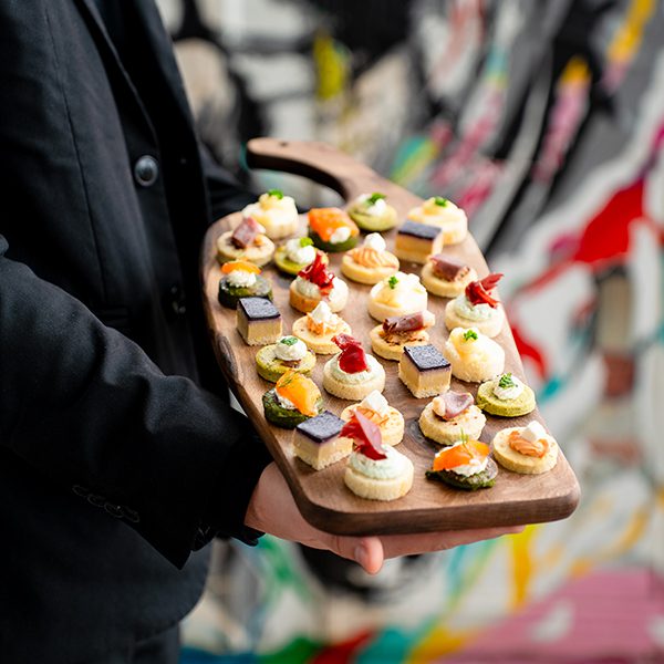 Maître d'hôtel présentant une belle planche en bois de pièces cocktails diverses.