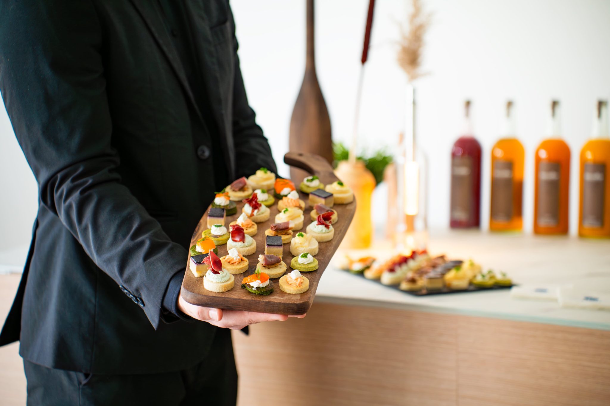 Maître d'hôtel très élégant tenant un plateaux en bois avec un assortiment de pièces cocktails.